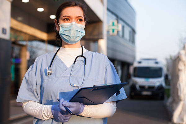 A nurse standing outside of a hospital with a clipboard in her hand