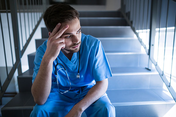 A nurse sitting on the steps looking stressed with his hand on his head