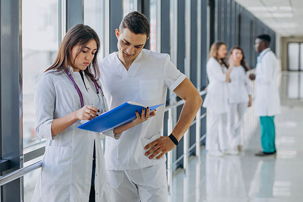 Two medical professionals looking at a patient's chart with other healthcare workers in the background
