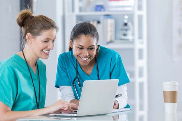 Two nurses looking at a laptop together and smiling