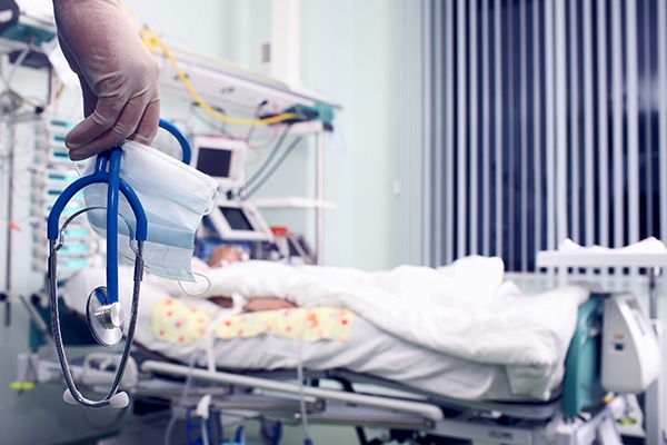 A nurse holding a medical mask and stethoscope in their hand while looking at a patient in their hospital bed