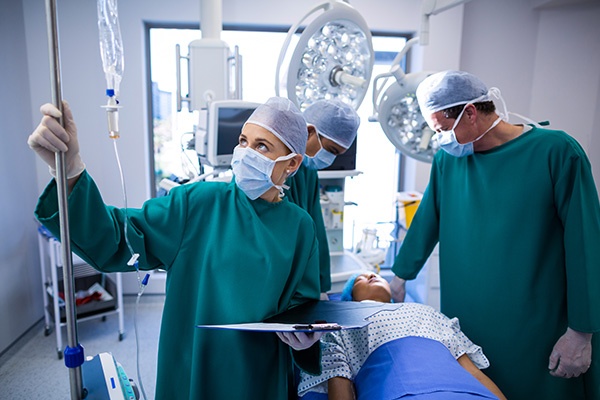 A nurse anesthetist looking at medications in an IV drip with other nurses looking at a patient on an operating table