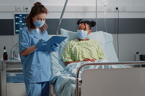 A nurse talking with a patient in their hospital bed while writing things on a clipboard