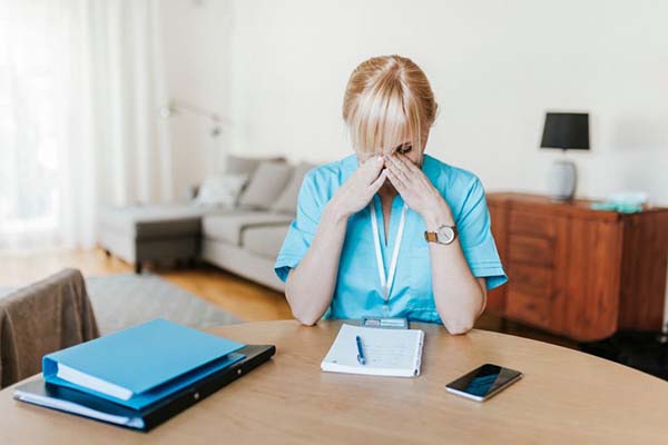 A nursing student with study materials nearby is taking a break with their head in their hands