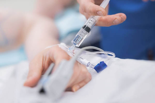 close up of a nurse pushing drugs from a syringe into an IV in someone's hand