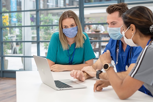 Nurses sitting around a laptop with masks on