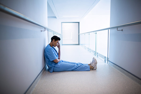 A nurse sitting on the floor of a hospital hallway looking sad