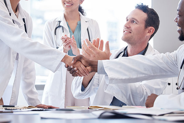 Medical professionals shaking hands while others applaud them