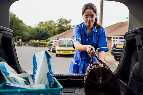 A travel nurse putting her suitcase into the trunk of a car