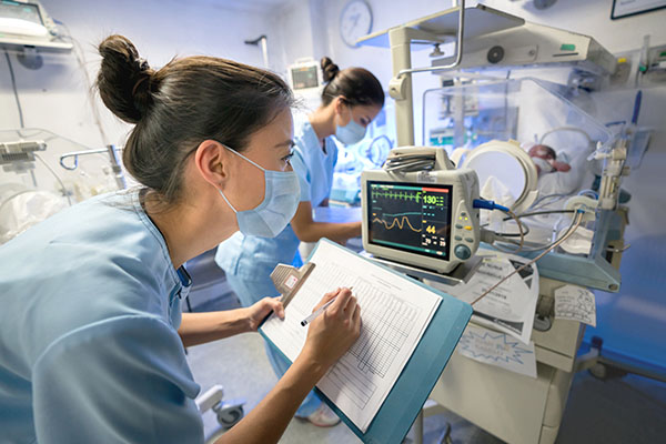 A CRNA charting information from a patient's medical machines in a hospital room