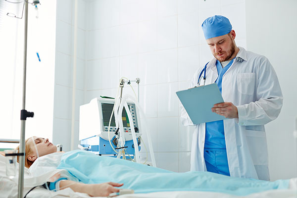A nurse anesthetist reviewing a chart standing near a patient in a hospital bed