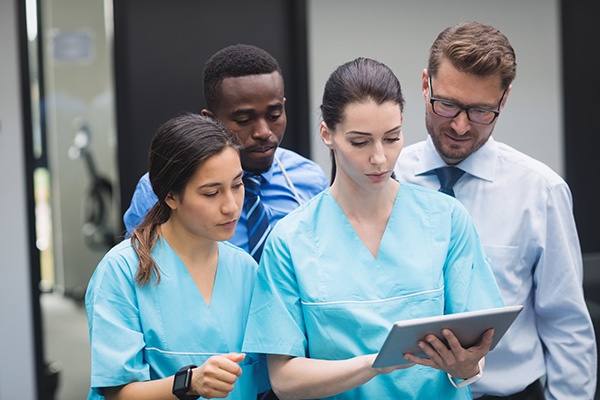 Four medical professionals standing together reviewing information on an iPad