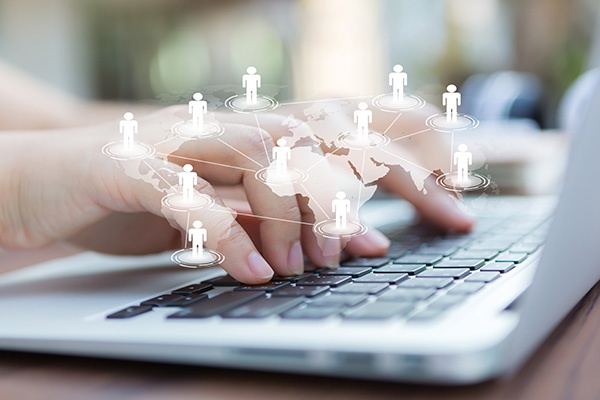 A person typing on a laptop with a graphic of connected people around the world overlayed on top of the image 