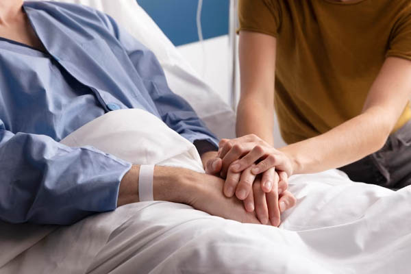 Close up of a person holding hands with a patient in a hospital bed