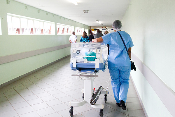 A nurse wheeling a newborn baby in a hospital carrier down the hallways