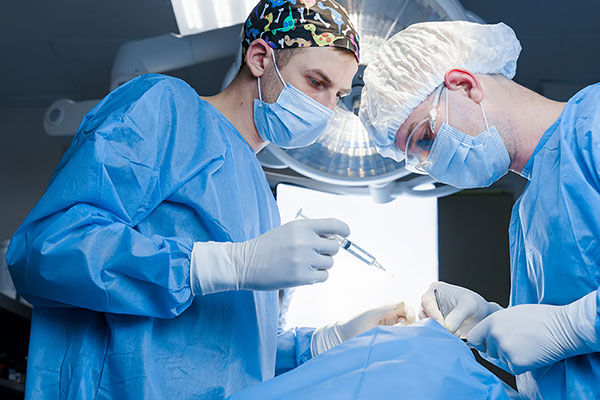 A nurse anesthetist with medication in their hand and another nurse leaning over a patient on an operating table 