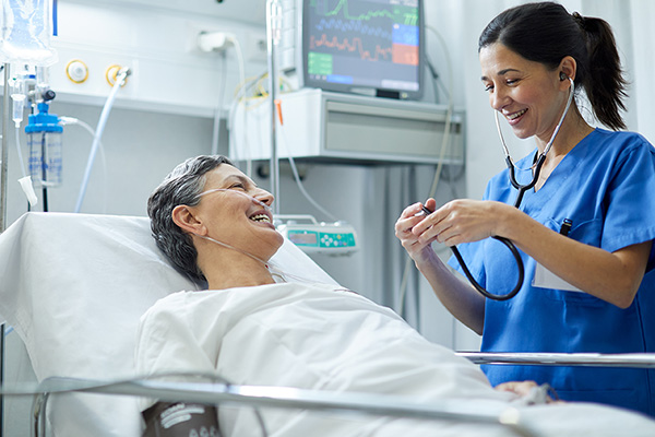 A nurse with a stethoscope talking to a patient who is laying in their hospital bed
