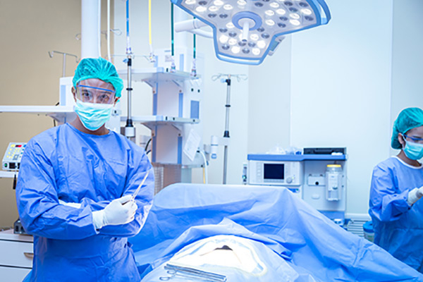 A CRNA in an operating room with a patient on the operating table and another nurse in the background