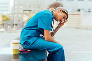 A nurse sitting on a bench outside with her head in her hands looking stressed