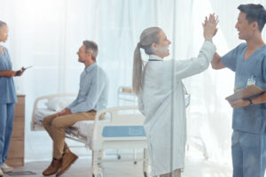 A nurse anesthetist high-fiving a nurse in a patient's hospital room while a doctor chats with the patient in the background