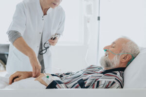A nurse taking the pulse of an older patient who is laying in their hospital bed