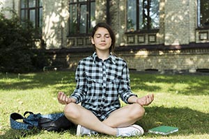 A student sitting on the lawn outside their university meditating
