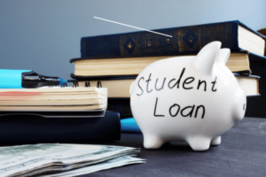 A photo of a piggy bank with the words Student Loan written on it; in the background are textbooks