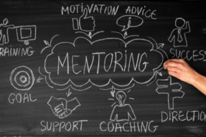 The word MENTORING is written on a chalkboard with other words surrounding it like COACHING and GOALS