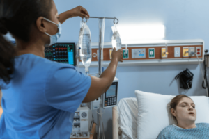 A female ICU nurse in a hospital room with a patient laying in a hospital bed