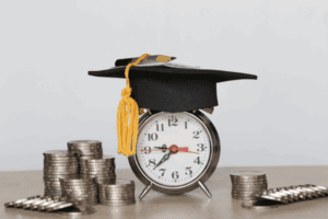 a graduation cap sitting on an alarm clock with money nearby 